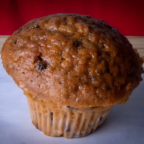 A large, golden-brown muffin with a crinkled paper liner sits against a red background.