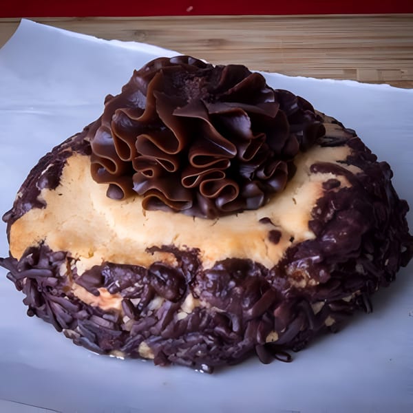 A chocolate-covered bagel with a large, ruffled chocolate swirl on top, on a white surface.