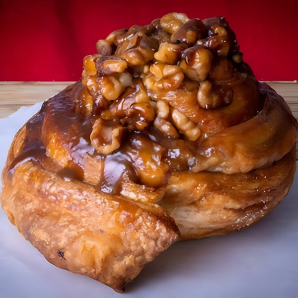 A sticky bun from House of Bagels, topped with glazed walnuts, on a white surface with a red background.